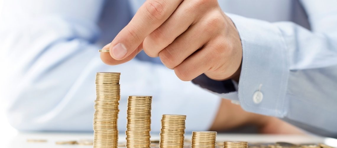 Savings, male hand stacking gold coins into increasing columns